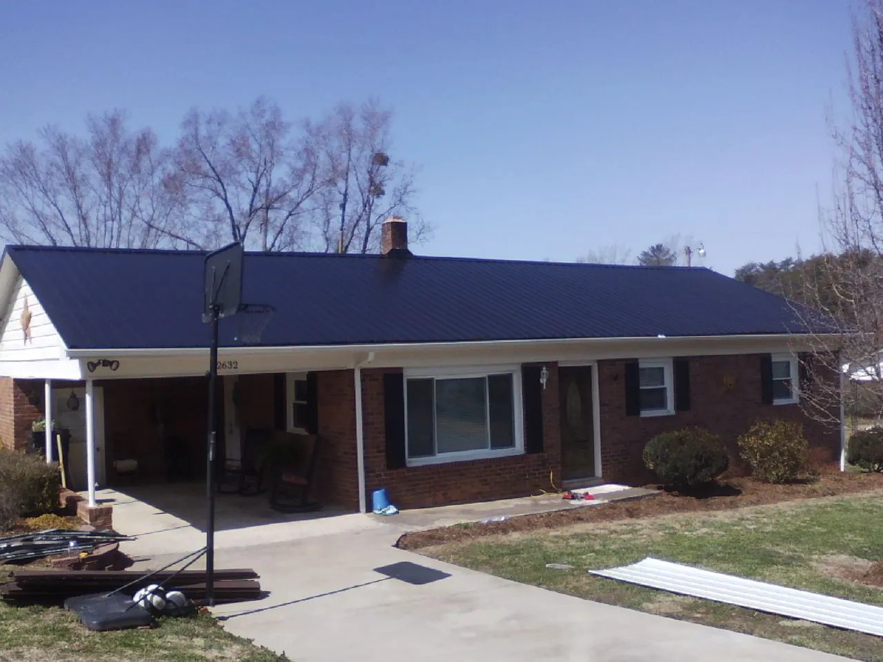 Finished dark blue metal roof on a brick ranch with a carport in Lansing