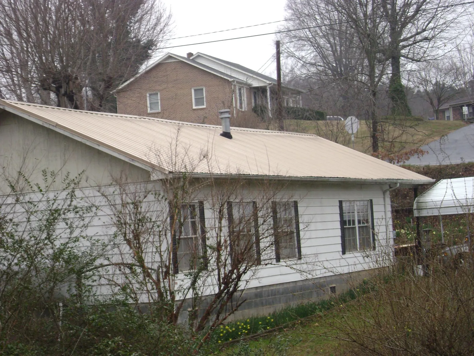 Tan metal roof on a white sided house set into a hillside — Commercial Roofing by Roofing Brothers in Lansing